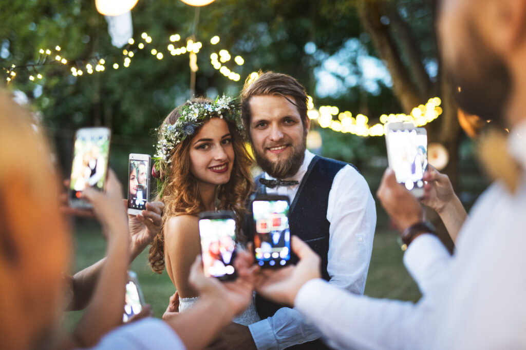 Hochzeitsgesellschaft macht Handyfotos von Braut und Bräutigam